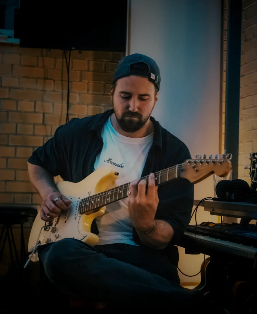 Michael Kümper playing an electric guitar, cap turned backwards, keyboard beside him